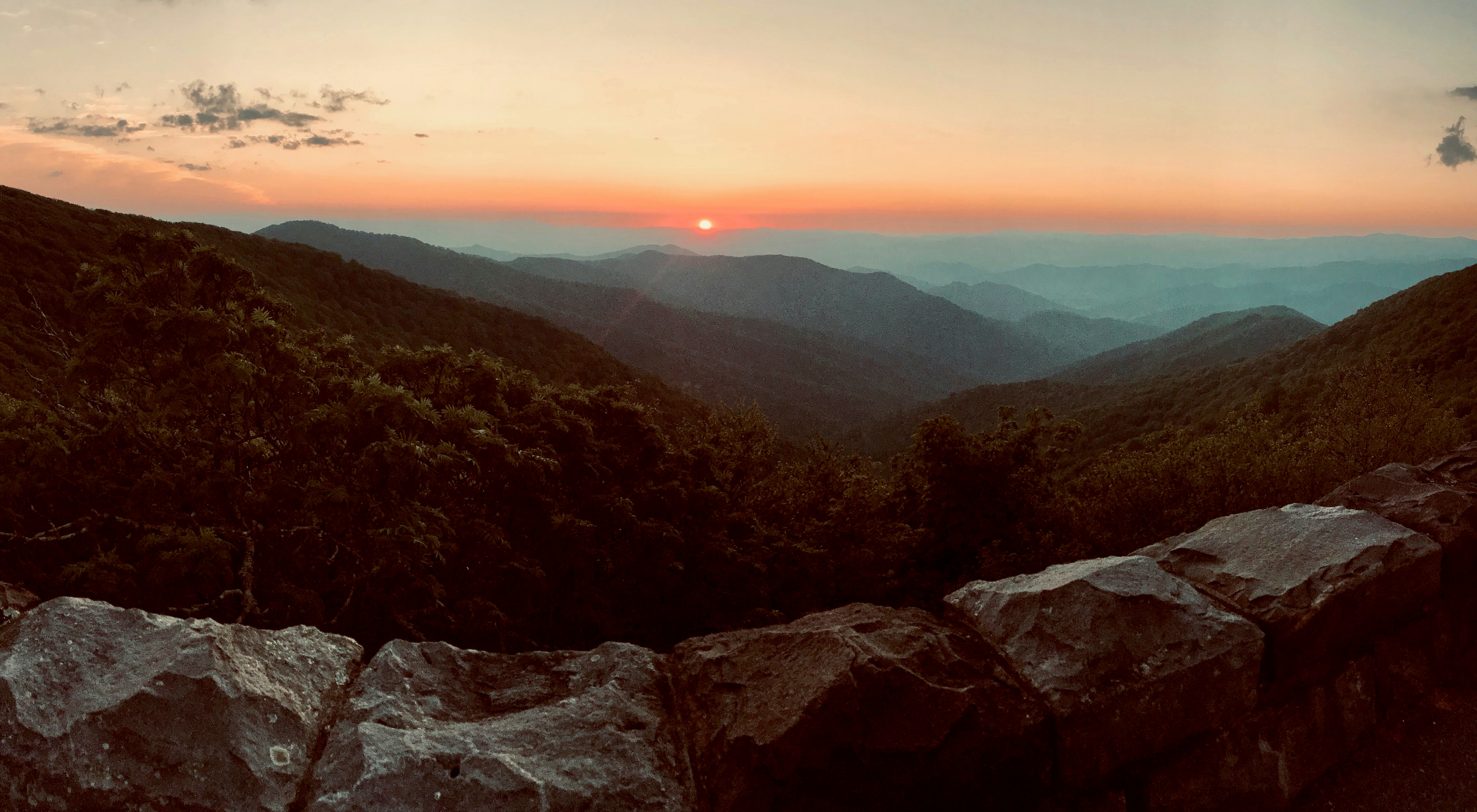 Mountain ridges at sunset with a warm sky and rocky foreground